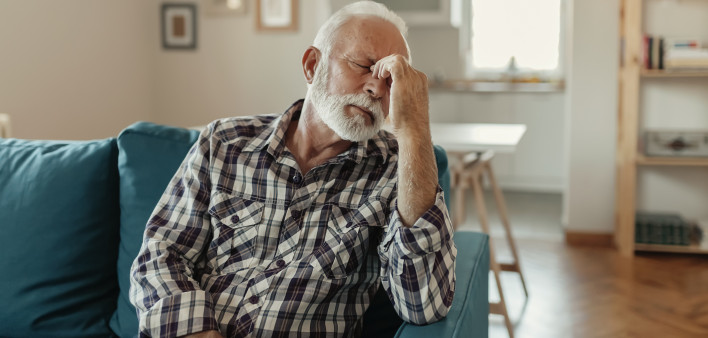 A Distraught Senior Man Suffering From a Migraine While Sitting on the sofa in the Living Room