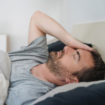 sick man lying down in bed and holding head