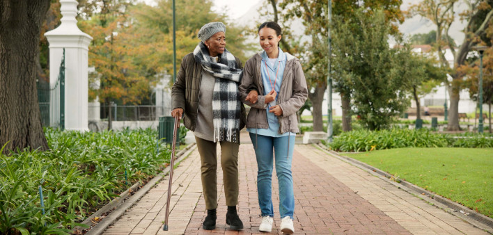 Help, cane and nurse with old woman in park for relax, support and person with a disability. Elderly care, conversation and healthcare with caregiver and patient in nature for medical rehabilitation